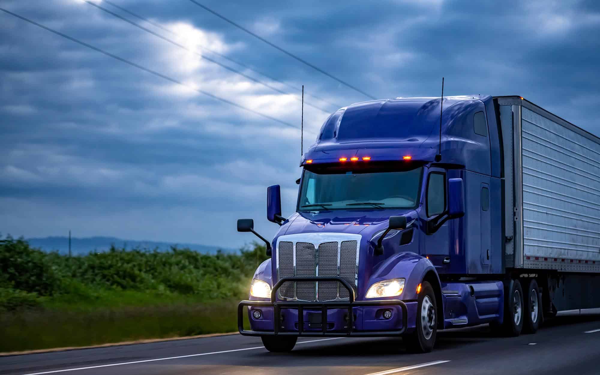 Side view of semi-truck driving down the road on a cloudy day