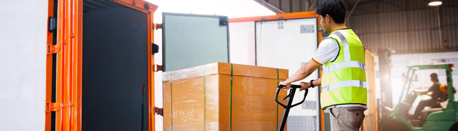 Side view of a young man loading a box onto a frieght truck using a pallet jack