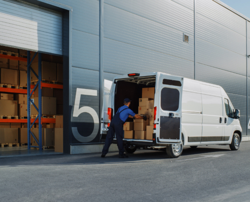 Outside of Logistics Retailer Warehouse With Female Manager Using Tablet Computer, Worker Loading Delivery Truck with Cardboard Boxes